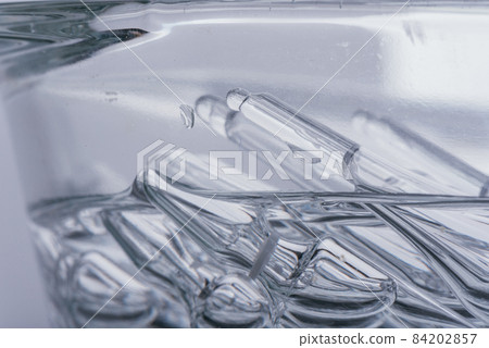 Glass medical ampoule vial for injection. Medicine is liquid sodium chloride with of aqueous solution in ampulla. Close up. Bottles ampule multicolor. 84202857