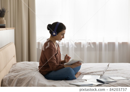 Indian woman sit on bed listen audio course studying remotely 84203737