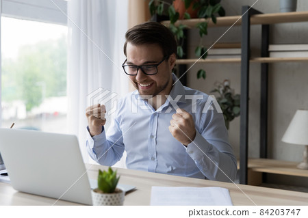 Happy young man in eyeglasses celebrating internet success. 84203747