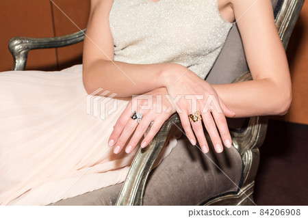 People, fashion, jewelry and luxury concept, closeup of woman wearing luxury jewelry sitting on armchair. Color gemstone ring and pendant with colored diamonds and gemstones 84206908