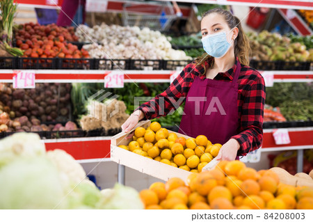 Young woman salesman in mask carrying box with plums Young woman salesman in mask carrying box with plums 84208003