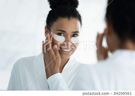Smiling young african american woman applying eyes patches. Smiling young african american woman applying eyes patches. 84209561