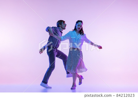 Couple of dancers, young man and woman in vintage retro style outfits dancing swing dance isolated on lilac color background in neon light Couple of dancers, young man and woman in vintage retro style outfits dancing swing dance isolated on lilac color background in neon light 84212023
