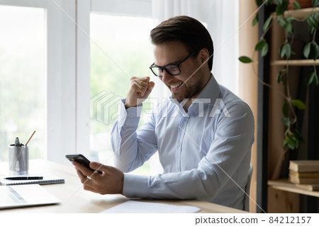 Happy emotional young man celebrating getting message with good news. 84212157