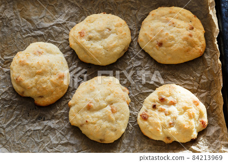 Dessert from cottage cheese with raisins. Cottage cheese pancakes baked in the oven on a background of parchment paper. Dessert from cottage cheese with raisins. Cottage cheese pancakes baked in the oven on a background of parchment paper. 84213969