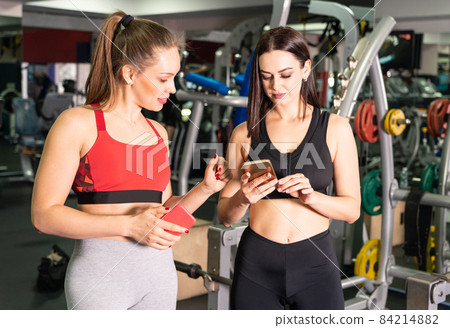 Two attractive fit women in gym with smart phone 84214882