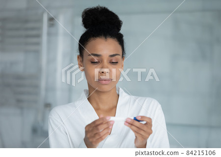 Concentrated young african mixed race woman using pregnancy test. Concentrated young african mixed race woman using pregnancy test. 84215106