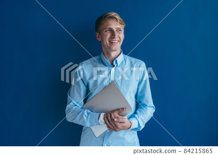 Portrait of young man in shirt holding laptop in his hands and smiling Portrait of young man in shirt holding laptop in his hands and smiling 84215865