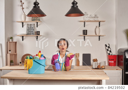 Woman wearing gloves, holding with a sponge in his hands, bowl full of bottles with disinfectant on table 84219502