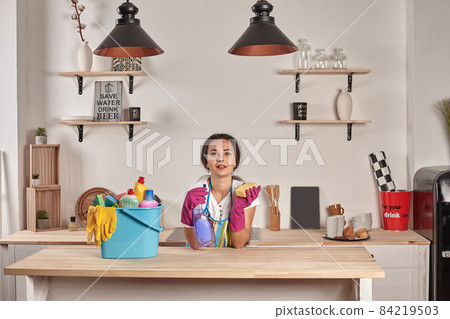 Woman wearing gloves, holding with a sponge in his hands, bowl full of bottles with disinfectant on table 84219503