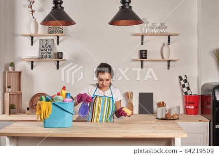 Woman wearing gloves, holding with a sponge in his hands, bowl full of bottles with disinfectant on table 84219509