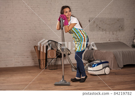 Young woman using vacuum cleaner in home living room floor, doing cleaning duties and chores, meticulous interior. Young woman using vacuum cleaner in home living room floor, doing cleaning duties and chores, meticulous interior. 84219782