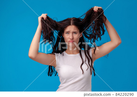 Sad woman is pulling her hair on blue background Sad woman is pulling her hair on blue background 84220290
