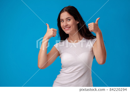 Smiling woman giving thumbs up on blue background Smiling woman giving thumbs up on blue background 84220294