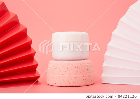 White cosmetic jar on pink gypsum podium against pink background decorated with red and white wavers. Luxury asian style skin care concept White cosmetic jar on pink gypsum podium against pink background decorated with red and white wavers. Luxury asian style skin care concept 84221120