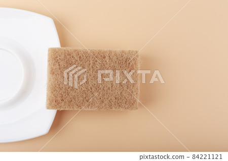 Dishwashing minimal creative concept in light beige colors. White ceramic plate and cleaning sponge top view 84221121