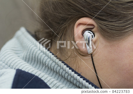 Close-up of woman ear with white earbud listenin to music Close-up of woman ear with white earbud listenin to music 84223783