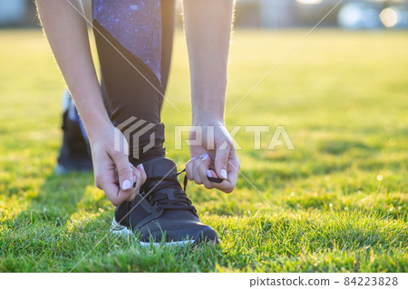 Close-up of female hands tying shoelace on running shoes before practice. Runner getting ready for training. Sport active lifestyle concept. Close-up of female hands tying shoelace on running shoes before practice. Runner getting ready for training. Sport active lifestyle concept. 84223828