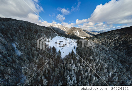 Aerial winter landscape with small rural houses between snow covered forest in cold mountains. 84224131