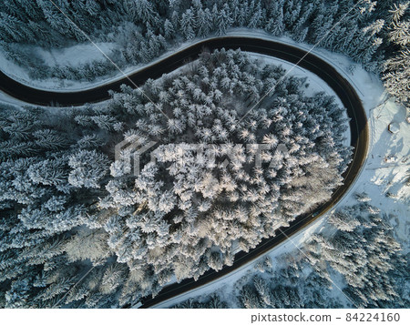 Aerial view of winter landscape with snow covered mountain hills and winding forest road in morning. 84224160