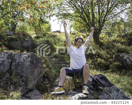 Man with smartphone is stretching. Orientation on terrain using built-in navigator application. Hiking with backpack in fall season. Bright autumn leaves. 84225124