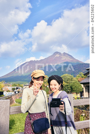A young woman and a friend taking a commemorative photo with Mt. Yufu in the background on a girls' trip A young woman and a friend taking a commemorative photo with Mt. Yufu in the background on a girls' trip 84225602