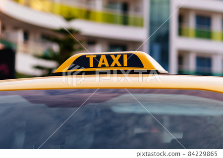 a taxi sign on the roof of a yellow car. 84229865