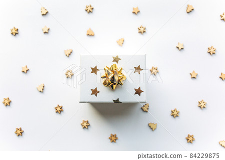 Gift white box with a gold ribbon with tinsel and wooden Christmas confetti on a white background. Gift concept, new year, festive background 84229875