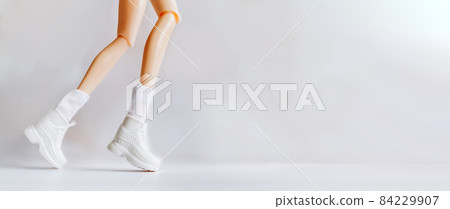 Physical activity and health. Doll's legs in white sneakers depicting running or movement Physical activity and health. Doll's legs in white sneakers depicting running or movement 84229907
