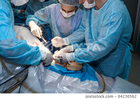 A team of surgeons stitches the patient's skin. 84230562