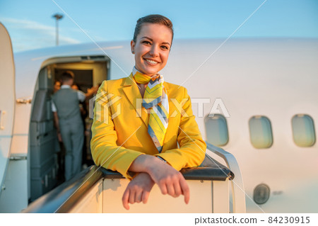 Cheerful flight attendant standing near aircraft door 84230915