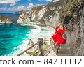 Woman wearing a red dress on standing on the stairs leading down at Diamond beach in Nusa Penida 84231112