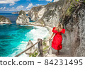 Back view woman wearing a red dress on standing on the stairs leading down at Diamond beach in Nusa 84231495
