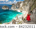 Back view woman wearing a red dress on standing on the stairs leading down at Diamond beach in Nusa 84232011