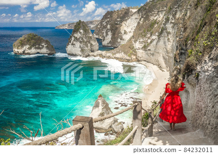 Back view woman wearing a red dress on standing on the stairs leading down at Diamond beach in Nusa 84232011