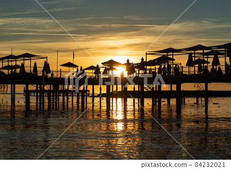 pier with umbrellas and sunbeds. silhouettes. beautiful sunset on sea.  84232021