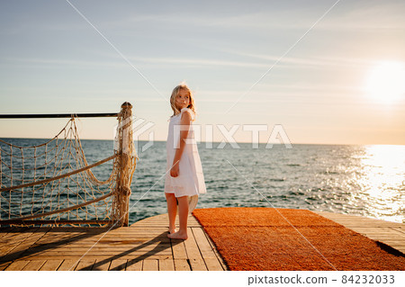 a little girl in a white dress by the sea on the pier 84232033