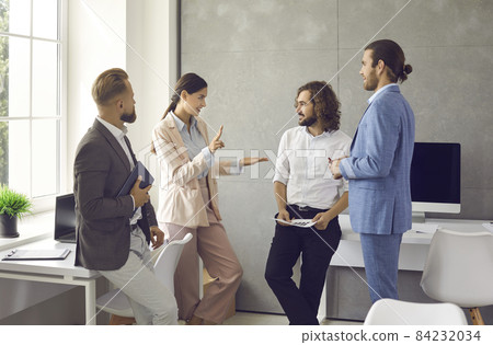 Group of young people standing in the office, having a work meeting and discussing a new business strategy. Female manager talking to a team of male employees or colleagues Group of young people standing in the office, having a work meeting and discussing a new business strategy. Female manager talking to a team of male employees or colleagues 84232034