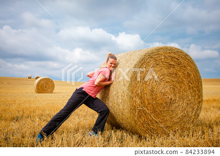 young woman pushing in a field of straw bales young woman pushing in a field of straw bales 84233894