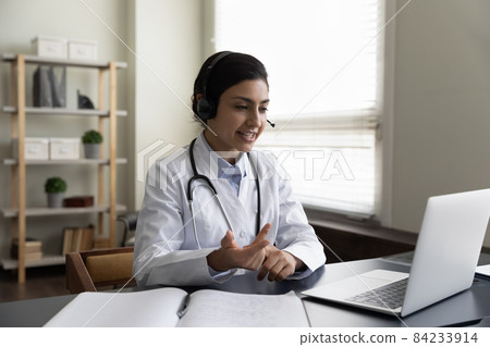 Indian woman doctor in wireless headphones talking, using laptop 84233914