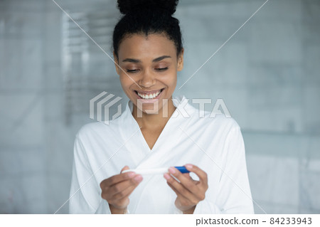 Happy interested young african mixed race woman using pregnancy test. Happy interested young african mixed race woman using pregnancy test. 84233943