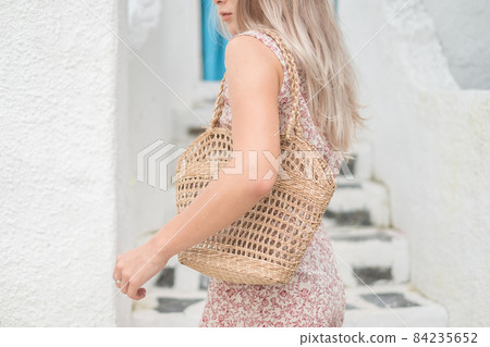 Picture of woven straw summer bag. Trendy summer outfit. Mock up. Blond woman in casual dress holding woven straw summer bag. High quality photo  84235652