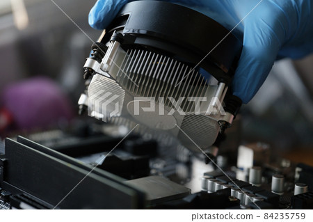 Person installing black cooler fan with copper tubes on computer processor 84235759