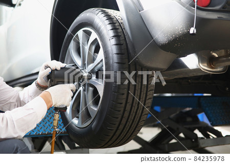 Automechanic with electric screwdriver changing tire in garage Automechanic with electric screwdriver changing tire in garage 84235978