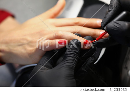 Professional salon worker cover clients nails with red colour polish Professional salon worker cover clients nails with red colour polish 84235983