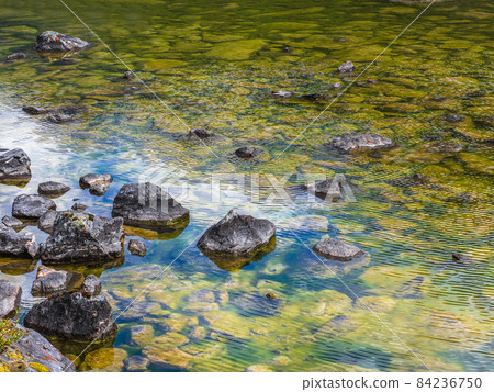 Beautiful nature background of stony bottom in turquoise transparent water. Glowing green natural background with a swamp surface. Scenery with wild flora of highlands in swampy mountain lake. 84236750