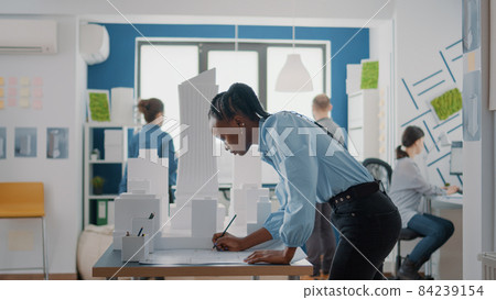 African american architect analyzing blueprints plan and building model to create project structure African american architect analyzing blueprints plan and building model to create project structure 84239154