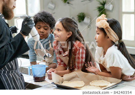 Children watching for the chef who making jam for cookies at the table during a lesson 84240354