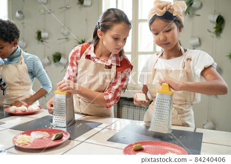 Little girl looking at the plate of her friend during cooking lesson in the kitchen Little girl looking at the plate of her friend during cooking lesson in the kitchen 84240406