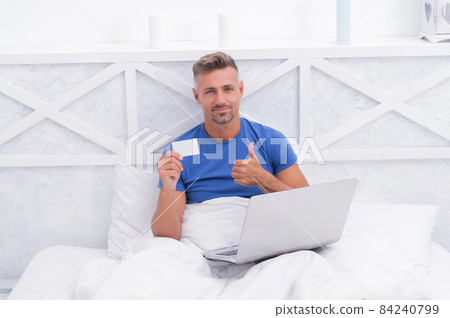 Purchasing something that delights me. Happy man shopping online in bed. Online shop Purchasing something that delights me. Happy man shopping online in bed. Online shop 84240799